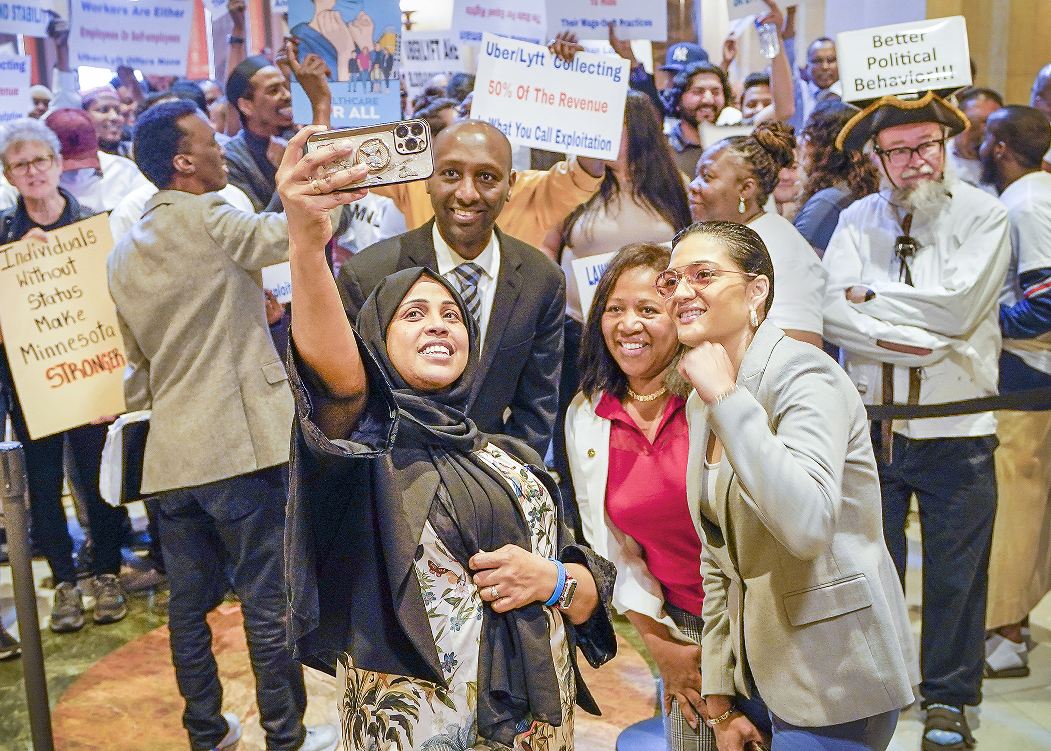 Rep. Hodan Hassan, Rep. Mohamud Noor, Rep. Mary Francis Clardy and Rep. Marìa Isa Pèrez-Vega pose for a selfie with supporters of HF2369 in front of the House Chamber May 17. (Photo by Andrew VonBank)